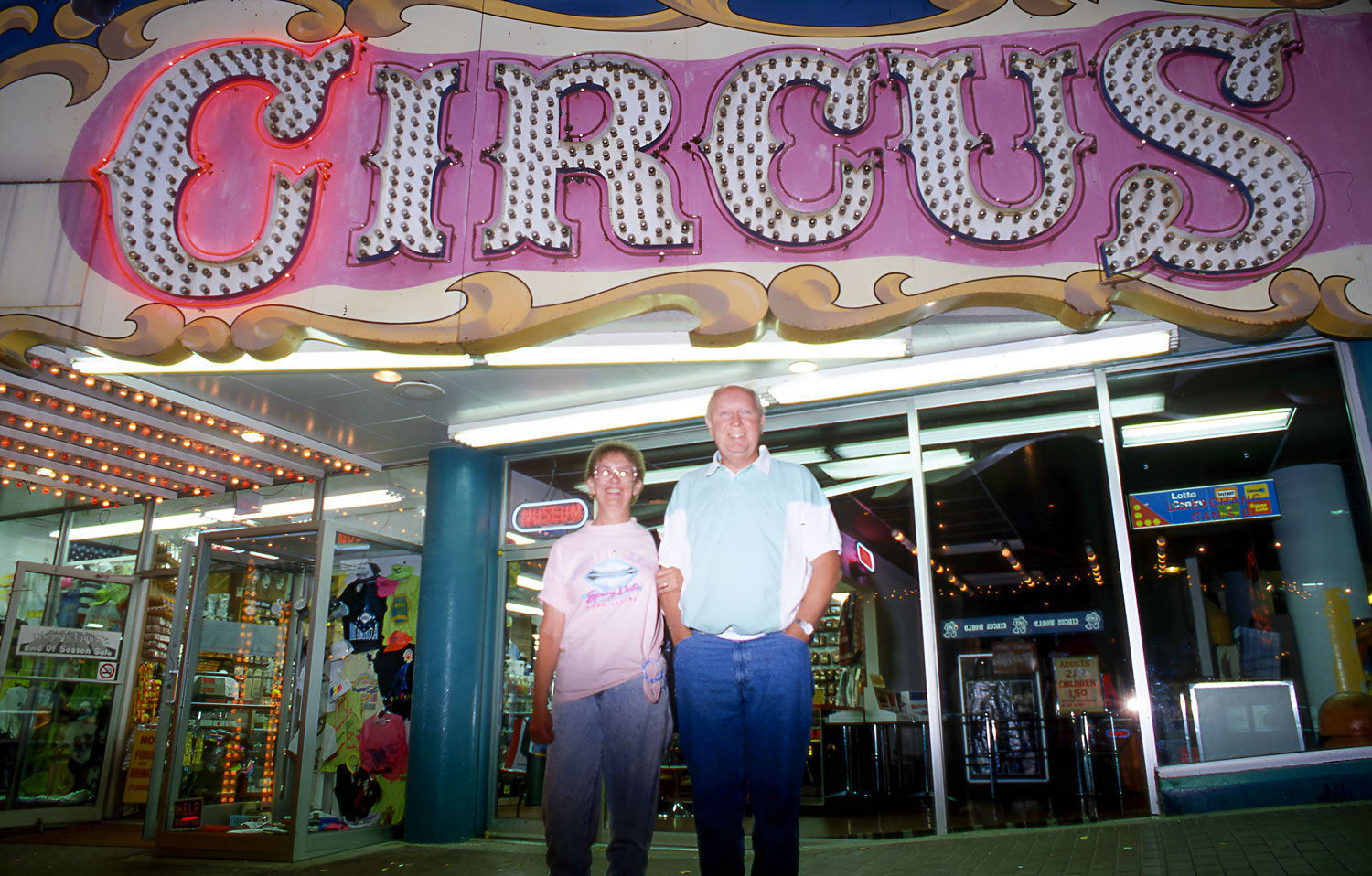 A couple poses for a photo beneath a glowing 'Circus' sign outside a tourist attraction in Niagara Falls.