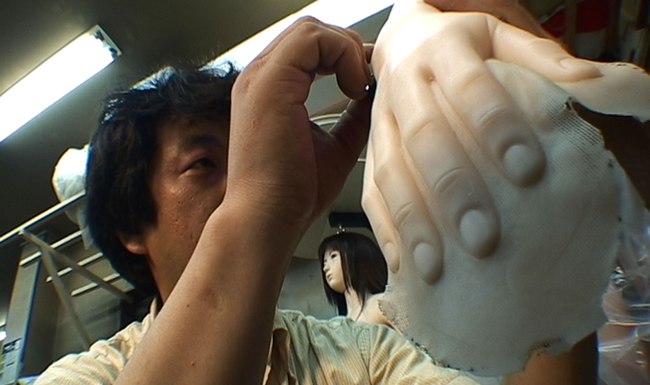 A craftsman works closely on the hand of a lifelike synthetic figure in a workshop.