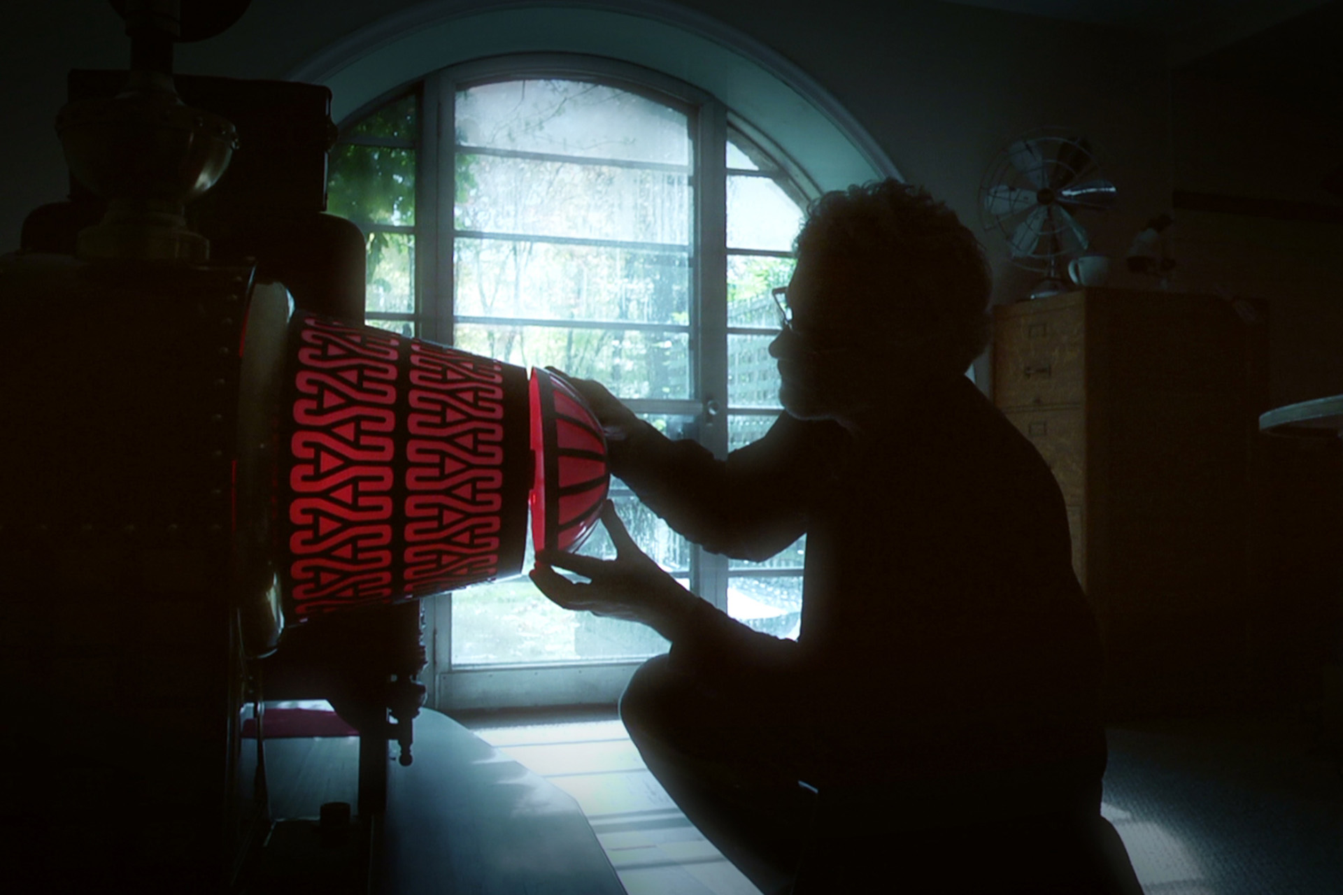 A silhouetted figure adjusts a large, ornate red and black cylindrical prop resembling a time machine.
